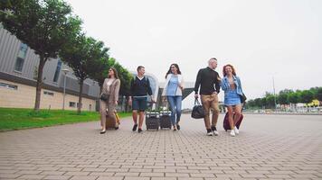 cinq en voyageant copains de retour de une voyage dans le Contexte de le aéroport avec bagage dans main. touristes sont les voyageurs qui avoir revenu de une voyage avec bagage à le aéroport. video