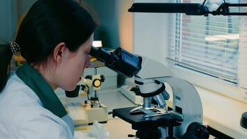 Female microbiologist looking for bacteria under a microscope. A researcher examines a variety of bacteria in the soil using a microscope. video