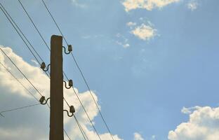 Old wooden electric pole for transmission of wired electricity on a background of a cloudy blue sky. Obsolete method of supplying electricity for later use photo