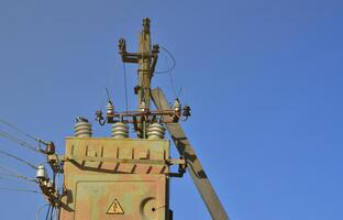 Old and obsolete electrical transformer against the background of a cloudless blue sky. Device for distribution of supply of high-voltage energy photo