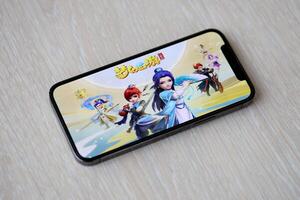Fantasy Westward Journey mobile iOS game on iPhone 15 smartphone screen on wooden table during mobile gameplay photo