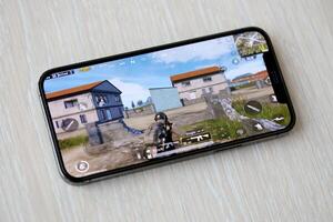 PUBG PlayerUnknowns Battlegrounds mobile iOS game on iPhone 15 smartphone screen on wooden table during mobile gameplay photo