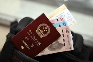 Red passport of People Republic of China and chinese yuan bills with airline tickets on backpack photo