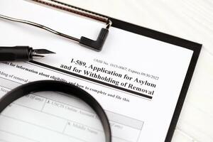 I-589 Application for asylum and for withholding of removal blank form on A4 tablet, lies on office table with pen and magnifying glass photo
