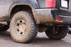 Wheel closeup in a countryside landscape with a mud road. Off-road 4x4 suv automobile with ditry body after drive in muddy road photo