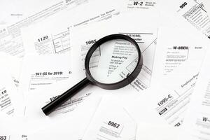 Magnifying glass lying over heap of paper documents. Investigation and financial audit photo