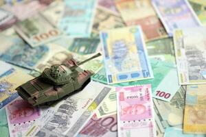 Small green tank on many banknotes of different currency. Background of war funding photo