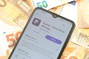 TERNOPIL, UKRAINE - AUGUST 3, 2023 PayPal application on screen on modern smartphone and many bills of euro currency photo