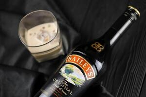 KYIV, UKRAINE - MAY 4, 2022 Baileys original alcohol bottle on wooden table with black fabric photo