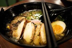 A bowl of ramen looks tempting with a golden yellow broth, topped with sliced tempura chicken, half-boiled egg, nori, mushrooms and finely chopped green onions. photo