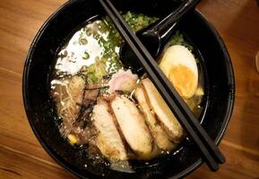 A bowl of ramen looks tempting with a golden yellow broth, topped with sliced tempura chicken, half-boiled egg, nori, mushrooms and finely chopped green onions. photo