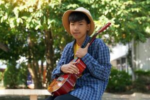 The Asian boy held the ukulele upright against his shoulder and placed it on his lap. Soft and selective focus. photo