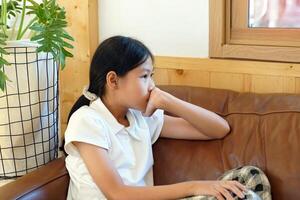 Asian girl sitting with her chin on the sofa. Her eyes are blurry, looking out the window Like a person who is sad Have a mental problem that cannot find a solution or solution. photo