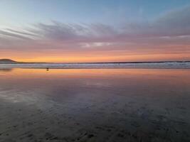 puesta de sol a playa Delaware famara, lanzarote, pinturas el cielo con vibrante matices, fundición un fascinante resplandor terminado el horizonte. asombroso visión ese capturas el esencia de tranquilidad y natural belleza. foto