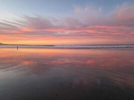 Sunset at Playa de Famara, Lanzarote, paints the sky with vibrant hues, casting a mesmerizing glow over the horizon. Breathtaking sight that captures the essence of tranquility and natural beauty. photo