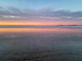 Sunset at Playa de Famara, Lanzarote, paints the sky with vibrant hues, casting a mesmerizing glow over the horizon. Breathtaking sight that captures the essence of tranquility and natural beauty. photo