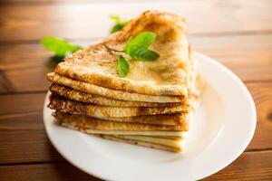 lot of thin pancakes in a plate, on wooden table. photo