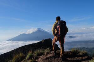 Asian Adventure, Man Model on Mountain Summit, Carrying Hiking Gear under Blue Sky above Ocean of Clouds photo