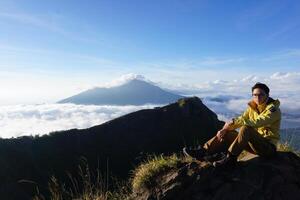 Skyward Summit, Asian Model on Mount Batur, Carrying Hiking Gear amidst Cloud Ocean photo