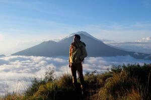 Asian Adventure, Man Model on Mountain Summit, Carrying Hiking Gear under Blue Sky above Ocean of Clouds photo