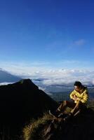 Asian Adventure, Man Model on Mountain Summit, Carrying Hiking Gear under Blue Sky above Ocean of Clouds photo