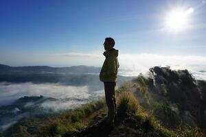 Asian Adventure, Man Model on Mountain Summit, Carrying Hiking Gear under Blue Sky above Ocean of Clouds photo