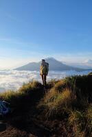 Asian Adventure, Man Model on Mountain Summit, Carrying Hiking Gear under Blue Sky above Ocean of Clouds photo