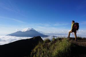 Asian Adventure, Man Model on Mountain Summit, Carrying Hiking Gear under Blue Sky above Ocean of Clouds photo