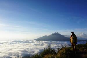 Asian Adventure, Man Model on Mountain Summit, Carrying Hiking Gear under Blue Sky above Ocean of Clouds photo