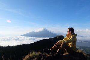 Asian Adventure, Man Model on Mountain Summit, Carrying Hiking Gear under Blue Sky above Ocean of Clouds photo