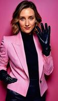 AI generated photo of middle aged woman with leather suit jacket and hand gloves standing against pink background, generative AI
