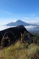 Asian Adventure, Man Model on Mountain Summit, Carrying Hiking Gear under Blue Sky above Ocean of Clouds photo