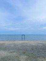 photo of a beach view with a cloudy sky and a swing in the middle of the beach