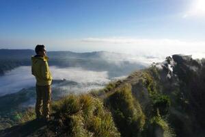 Asian Adventure, Man Model on Mountain Summit, Carrying Hiking Gear under Blue Sky above Ocean of Clouds photo