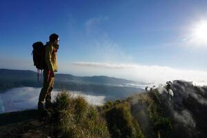 Asian Adventure, Man Model on Mountain Summit, Carrying Hiking Gear under Blue Sky above Ocean of Clouds photo