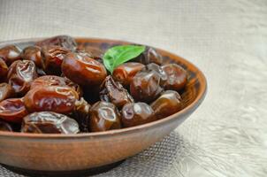 Dates in a brown plate on a textured light background, side view photo