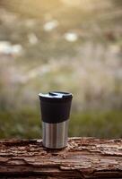 Vertical shot of a travel mug on a log over blurred nature background with copy advertising space photo