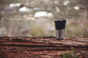 Horizontal shot of a travel mug on a log over blurred nature background with copy advertising space photo