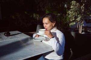 retrato de un hermosa mujer Bebiendo recién elaborada café en al aire libre cafetería, disfrutando desayuno antes de yendo a trabajo foto