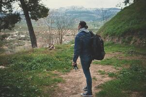 Full size dramatic shot of a hiker young man with backpack standing in the forest path and looking at the mountains photo