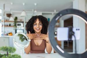 Happy young caucasian woman streaming a beauty vlog from home, online content creator applying a makeup showing cosmetic procedure at home in bedroom interior. photo