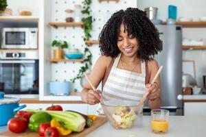 Happy smiling cute woman is preparing a fresh healthy vegan salad with many vegetables in the kitchen at home and trying a new recipe photo