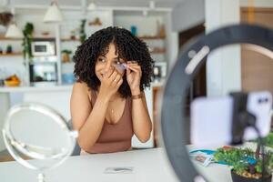 Happy young caucasian woman streaming a beauty vlog from home, online content creator applying a makeup showing cosmetic procedure at home in bedroom interior. photo