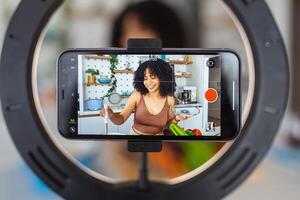un hermosa africano americano mujer comida blogger o vlogger grabación un vídeo en teléfono inteligente foto