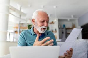 Surprised laughing happy old mature retired man looking through paper document, feeling excited analyzing financial information, getting taxes refund or bank loan approval at home. photo