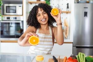 Beautiful young woman drinking fresh orange juice in kitchen. Healthy diet. Happy young woman with glass of juice and orange at table in kitchen. photo