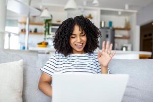 sonriente mujer trabajo en línea en computadora a hogar saludar ola hablar hablar en vídeo llamada en dispositivo. contento hembra utilizar ordenador portátil tener cámara web vídeo virtual evento con cliente o maestro. foto