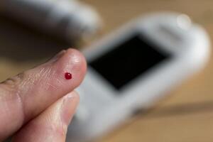 Woman pricking her finger to check blood glucose level with glucometer, test blood glucose for diabetes photo