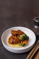 Plate of beef ribs in barbecue sauce with vegetables and mashed potatoes on dark background photo