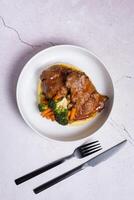 Plate of beef ribs in red sauce with vegetables and mashed potatoes with black cutlery top view, flat lay photo